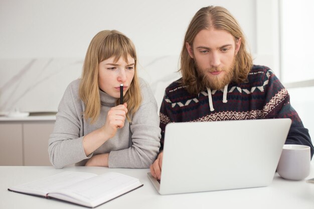 Retrato de una joven pareja pensativa sentada y trabajando en una laptop juntos en casa