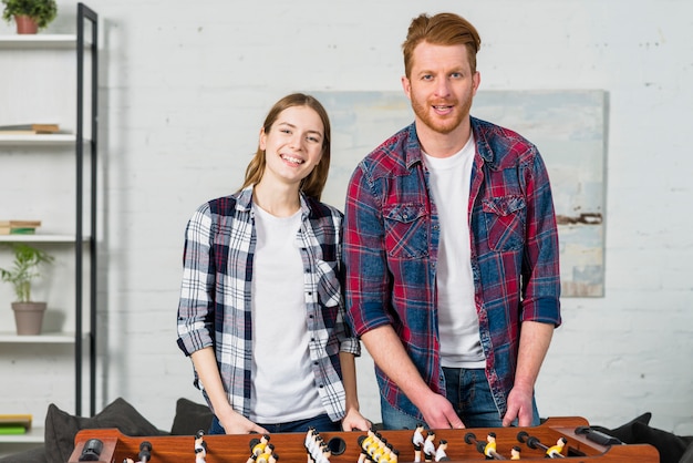 Foto gratuita retrato de joven pareja de pie detrás de la mesa de juego de fútbol en la sala de estar