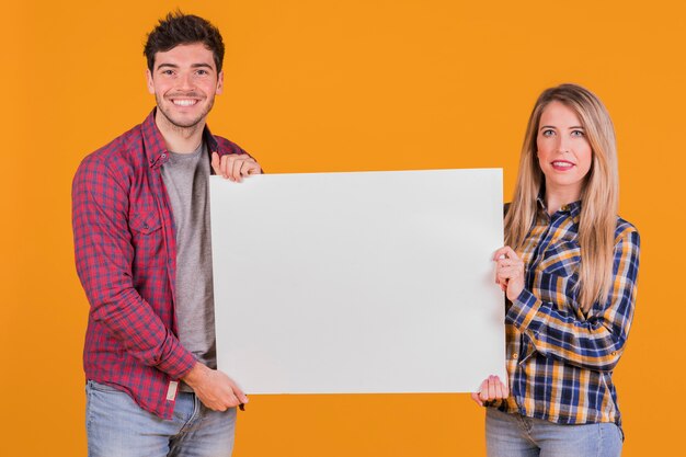 Retrato de una joven pareja que presenta un cartel blanco sobre un fondo naranja