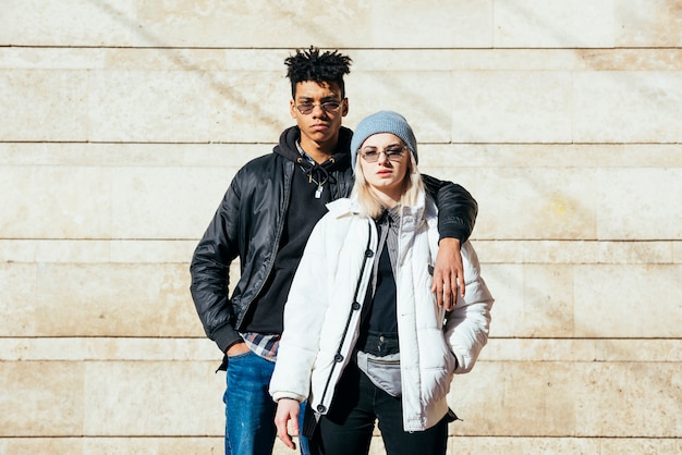 Retrato de joven pareja en ropa de moda de pie contra la pared