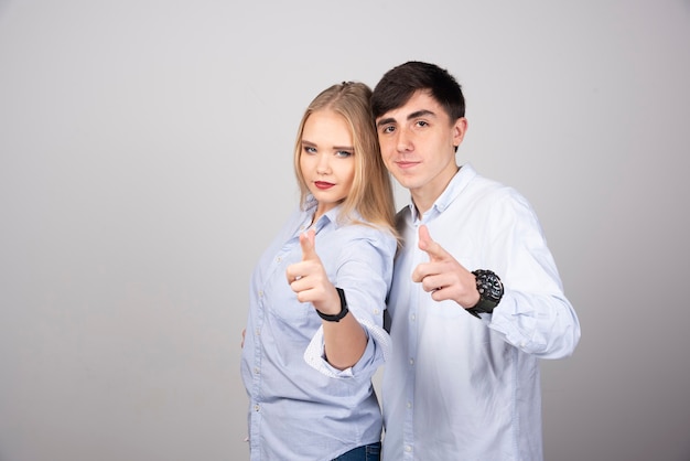 Retrato de una joven pareja señalando con el dedo aislado sobre la pared gris.