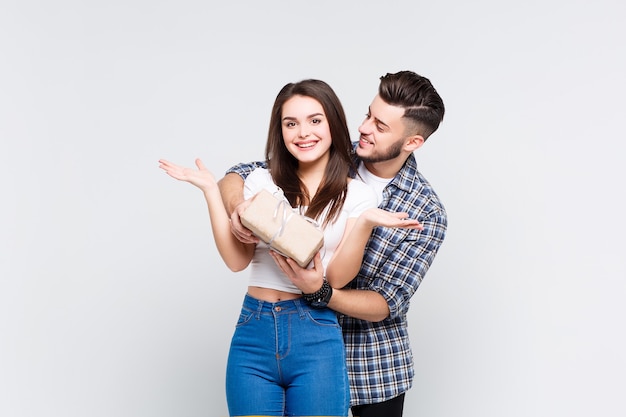 Foto gratuita retrato de una joven pareja sonriente abrazándose mientras está de pie junto con un cuadro actual sobre una pared blanca