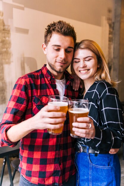 Retrato de una joven pareja sonriente animando los vasos de cerveza