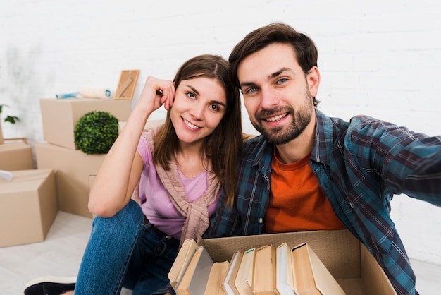 Retrato de una joven pareja sonriente con libros en la caja de cartón tomando sulfuro