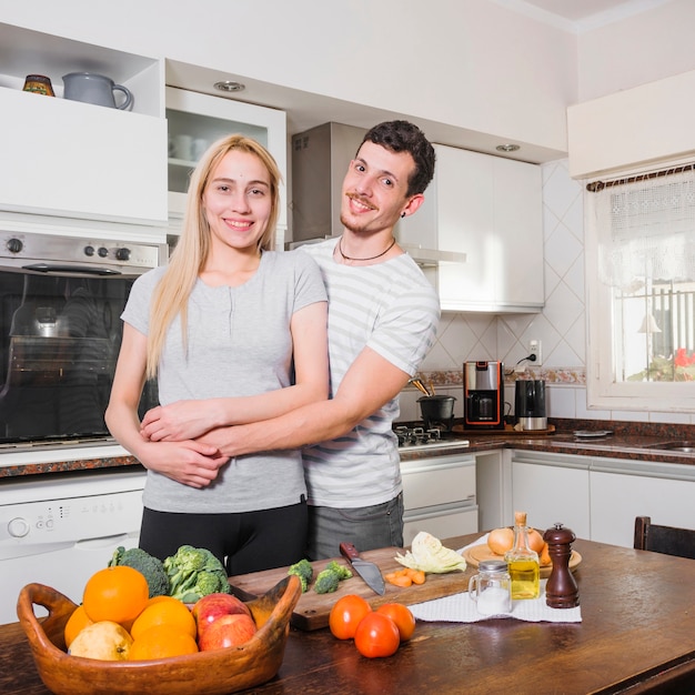 Retrato de una joven pareja sonriente de pie detrás de la mesa con muchas verduras de colores