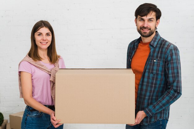 Retrato de una joven pareja sonriente sosteniendo una caja de cartón en la mano mirando a la cámara