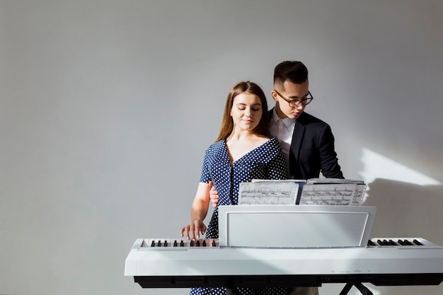 Retrato de joven pareja tocando el piano juntos contra la pared gris