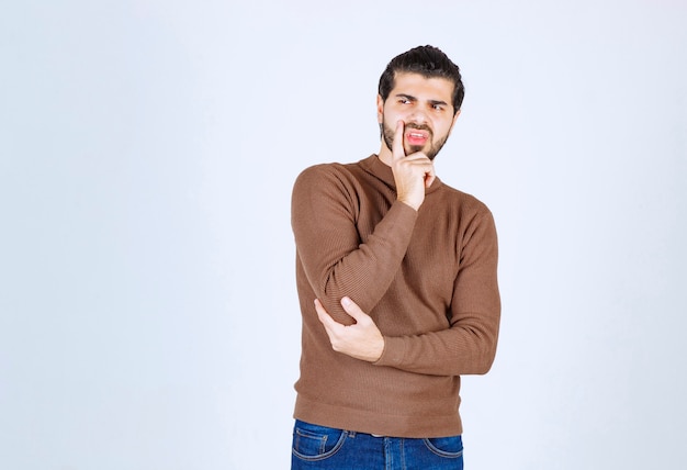 Retrato de un joven pensando y de pie contra la pared blanca.