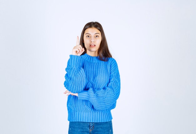 Retrato de una joven pensativa de pie y apuntando hacia arriba.