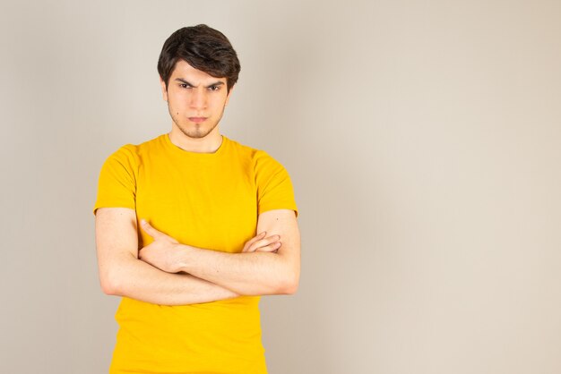 Retrato de un joven de pie con los brazos cruzados contra el gris.