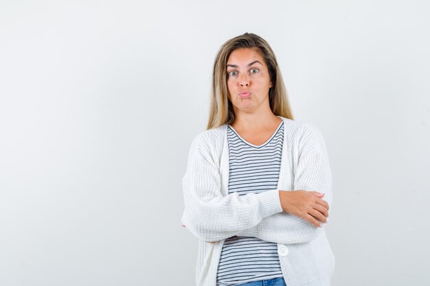 Retrato de joven de pie con los brazos cruzados, haciendo pucheros con los labios en camiseta, chaqueta y mirando perplejo vista frontal