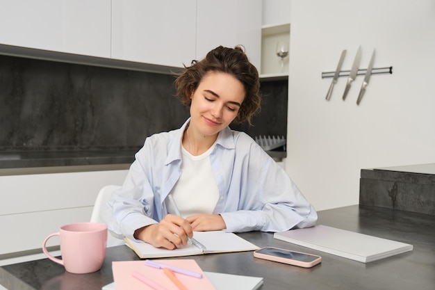 Retrato de una joven que trabaja desde casa escribiendo información en un cuaderno tomando notas sentada