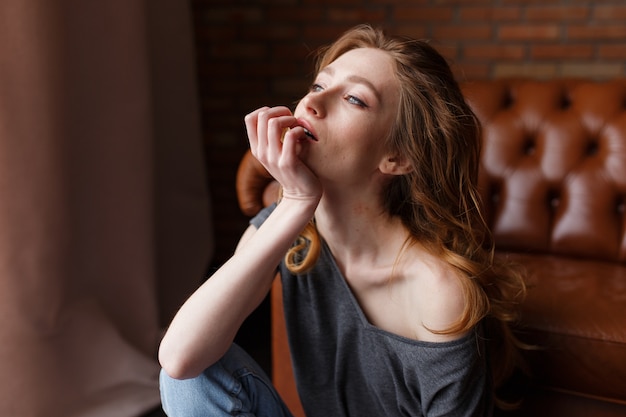 Retrato de joven redhair mujer sentada en el sofá de cuero marrón.