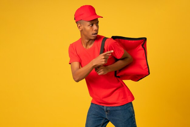 Retrato de joven repartidor vestido con un uniforme rojo corriendo sobre antecedentes aislados. Concepto de entrega.