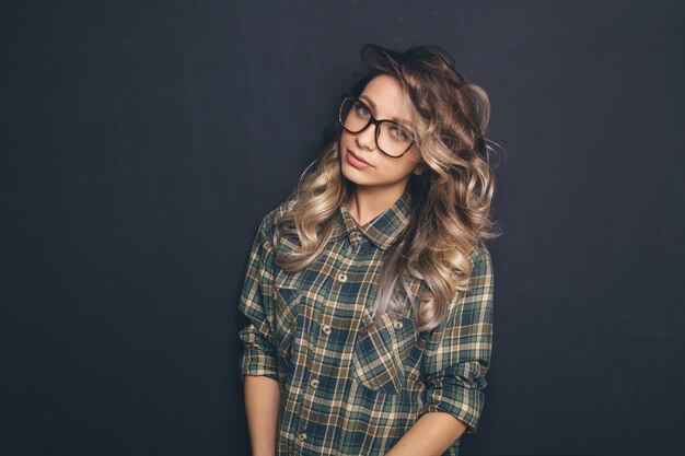 Retrato de una joven rubia hermosa con gafas de moda y ropa casual y posando sobre fondo negro