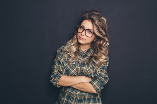 Retrato de una joven rubia hermosa con gafas de moda y ropa casual y posando sobre fondo negro