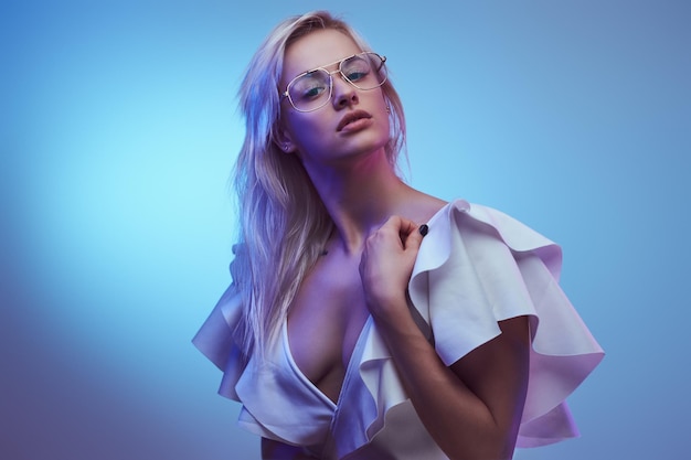 Retrato de una joven seductora con gafas y elegante traje blanco. aislado en un fondo azul
