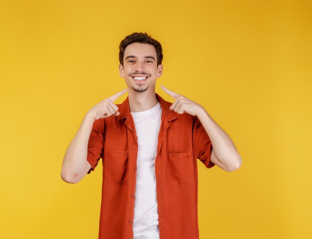 Retrato de un joven señalando con el dedo el espacio de copia aislado en el fondo amarillo del estudio