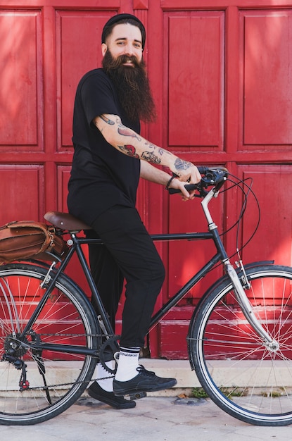 Retrato de un joven sentado en la bicicleta contra la puerta roja