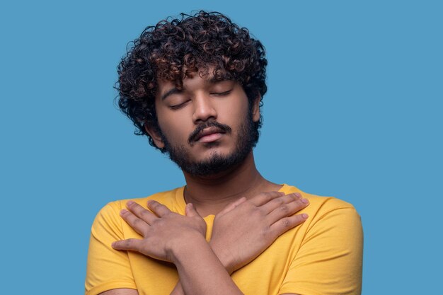 Retrato de un joven sereno con los ojos cerrados de pie contra el fondo azul.