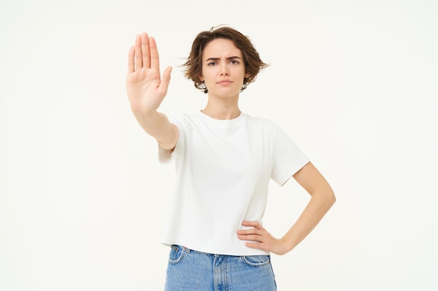 Foto gratuita retrato de una joven seria y segura de sí misma extiende una mano y muestra un gesto de parada de desaprobación