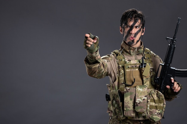 Retrato de joven soldado de camuflaje con ametralladora en la pared oscura