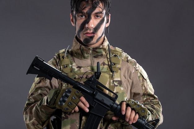 Foto gratuita retrato de joven soldado de camuflaje con ametralladora en la pared oscura