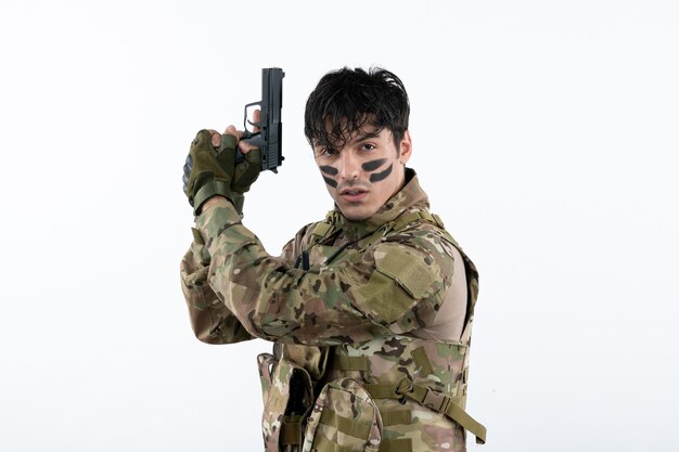 Retrato, de, joven, soldado, en, camuflaje, con, arma de fuego, en, pared blanca