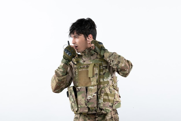 Retrato de joven soldado en camuflaje hablando a través de la pared blanca de walkie-talkie