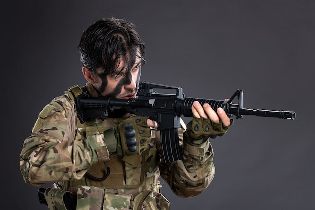 Retrato de joven soldado en camuflaje con el objetivo de ametralladora en la pared oscura