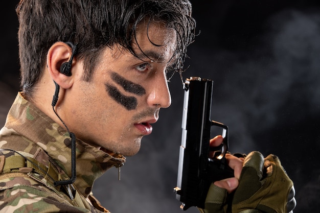 Retrato de joven soldado de camuflaje con el objetivo de pistola en la pared negra