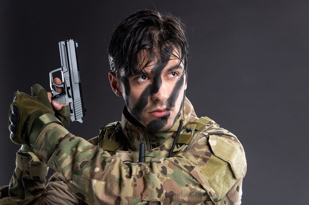 Retrato de joven soldado de camuflaje con el objetivo de pistola en la pared oscura
