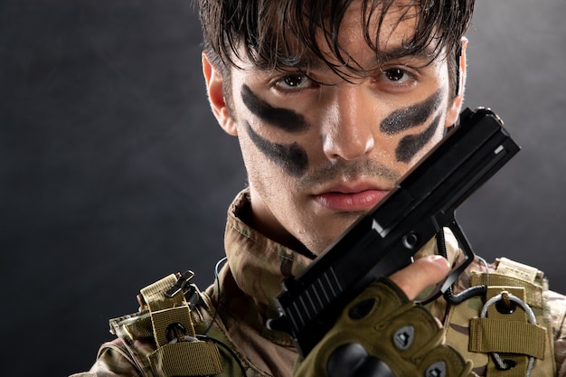 Retrato de joven soldado de camuflaje con pistola en pared negra