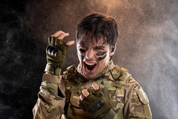 Retrato de joven soldado gritando de uniforme en la pared oscura