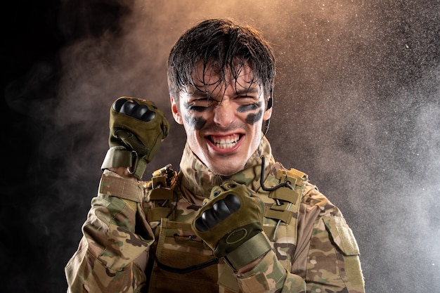 Retrato de joven soldado regocijándose en uniforme en la pared oscura