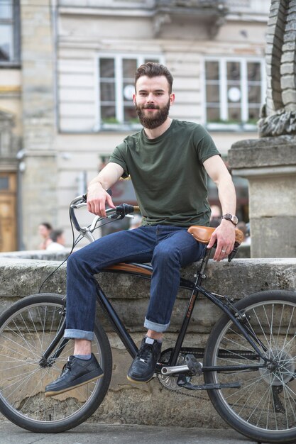 Retrato de un joven sonriente con bicicleta en la ciudad