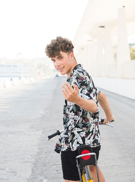 Retrato de un joven sonriente con bicicleta haciendo gesto con la mano