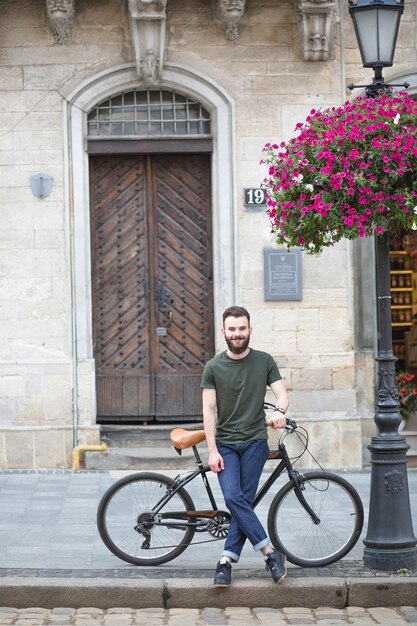 Retrato de un joven sonriente con bicicleta de pie sobre el pavimento