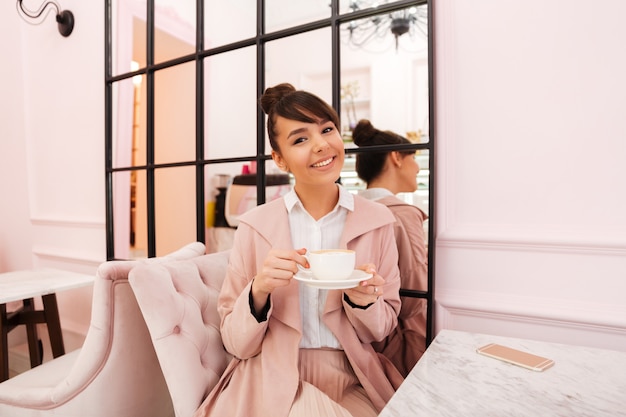 Retrato de una joven sonriente en chaqueta rosa tomando café