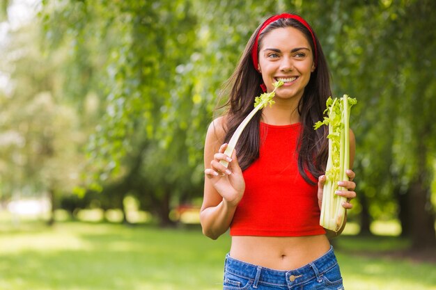 Retrato de joven sonriente, comiendo apio fresco en el parque