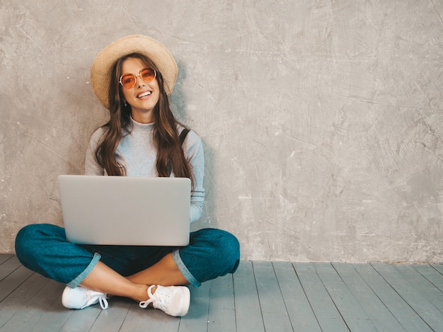 Foto gratuita retrato de joven sonriente creativa en gafas de sol. hermosa niña sentada en el piso cerca de la pared gris.