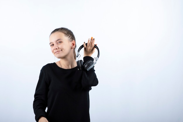 Retrato de una joven sonriente modelo sosteniendo auriculares en la mano