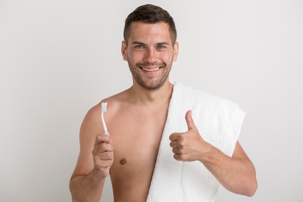 Retrato de joven sonriente mostrando pulgar arriba gesto mientras sostiene el cepillo de dientes