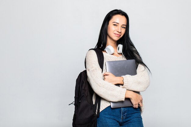 Retrato de una joven sonriente de pie con la computadora portátil contra la pared gris