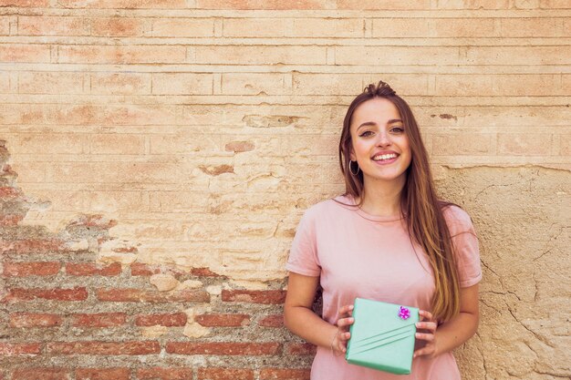 Retrato de una joven sonriente con regalo delante de la antigua muralla