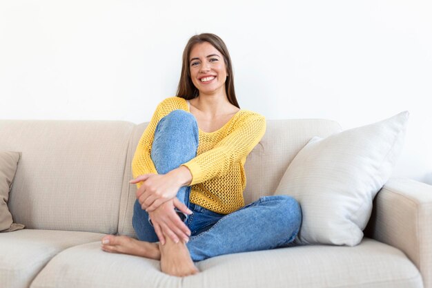 Retrato de una joven sonriente relajándose sola en el sofá de su sala de estar en casa por la tarde