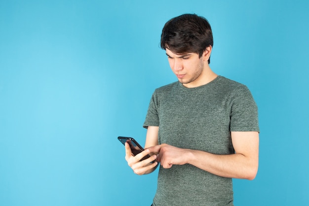 Retrato de un joven con un teléfono móvil contra el azul.