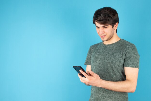 Retrato de un joven con un teléfono móvil contra el azul.