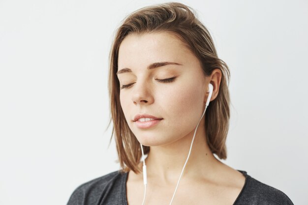 Retrato de joven tierna escucha música en auriculares con los ojos cerrados.