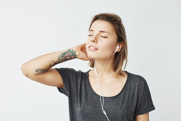 Retrato de joven tierna escucha música en auriculares con los ojos cerrados.